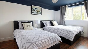 Un dormitorio con dos camas, un ventanal con cortinas, una lámpara de techo y una obra de arte colgada en la pared.
