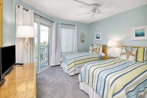 A hotel room with two beds, a TV, a ceiling fan, and a balcony with curtains. - Spacious, Oceanfront Condominium (Saint Simons Island)