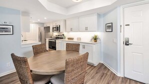 A modern kitchen with white cabinets, a round dining table, wicker chairs, and a built-in microwave. - Spacious, Oceanfront Condominium (Saint Simons Island)