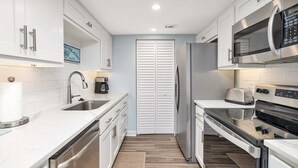 A modern kitchen with white cabinetry, stainless steel appliances, and a wooden floor. - Spacious, Oceanfront Condominium (Saint Simons Island)