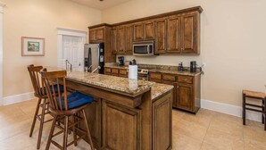 Una cocina con armarios de madera, encimera de granito, refrigerador, microondas y cafetera.