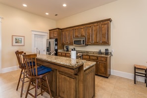 Kitchen features a central island with bar stools, a refrigerator, microwave, and coffee maker.