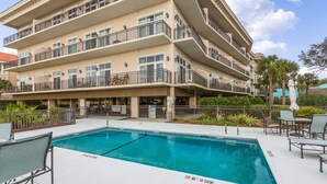 Un hotel de varios pisos con piscina, mobiliario exterior y balcones.