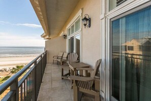 A balcony with a view of the beach, featuring a table and chairs, and a railing.