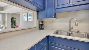 A kitchen with blue cabinets, a stainless steel sink, and a coffee maker on the counter. - St Simons Family Friendly Beachfront Condominium! (Saint Simons Island)