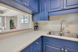 A kitchen with blue cabinets, a stainless steel sink, and a coffee maker on the counter. - St Simons Family Friendly Beachfront Condominium! (Saint Simons Island)