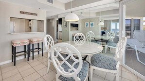 A dining area with a round table and white chairs, a kitchen area, and a balcony with a view. - St Simons Family Friendly Beachfront Condominium! (Saint Simons Island)