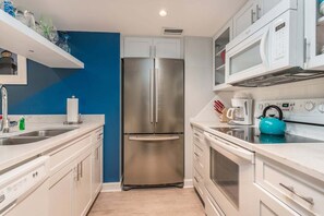 A modern kitchen with white cabinets, a stainless steel refrigerator, a microwave, and a kettle on the countertop. - Oceanfront Condo with Balcony, Pool Beach Access (Saint Simons Island)