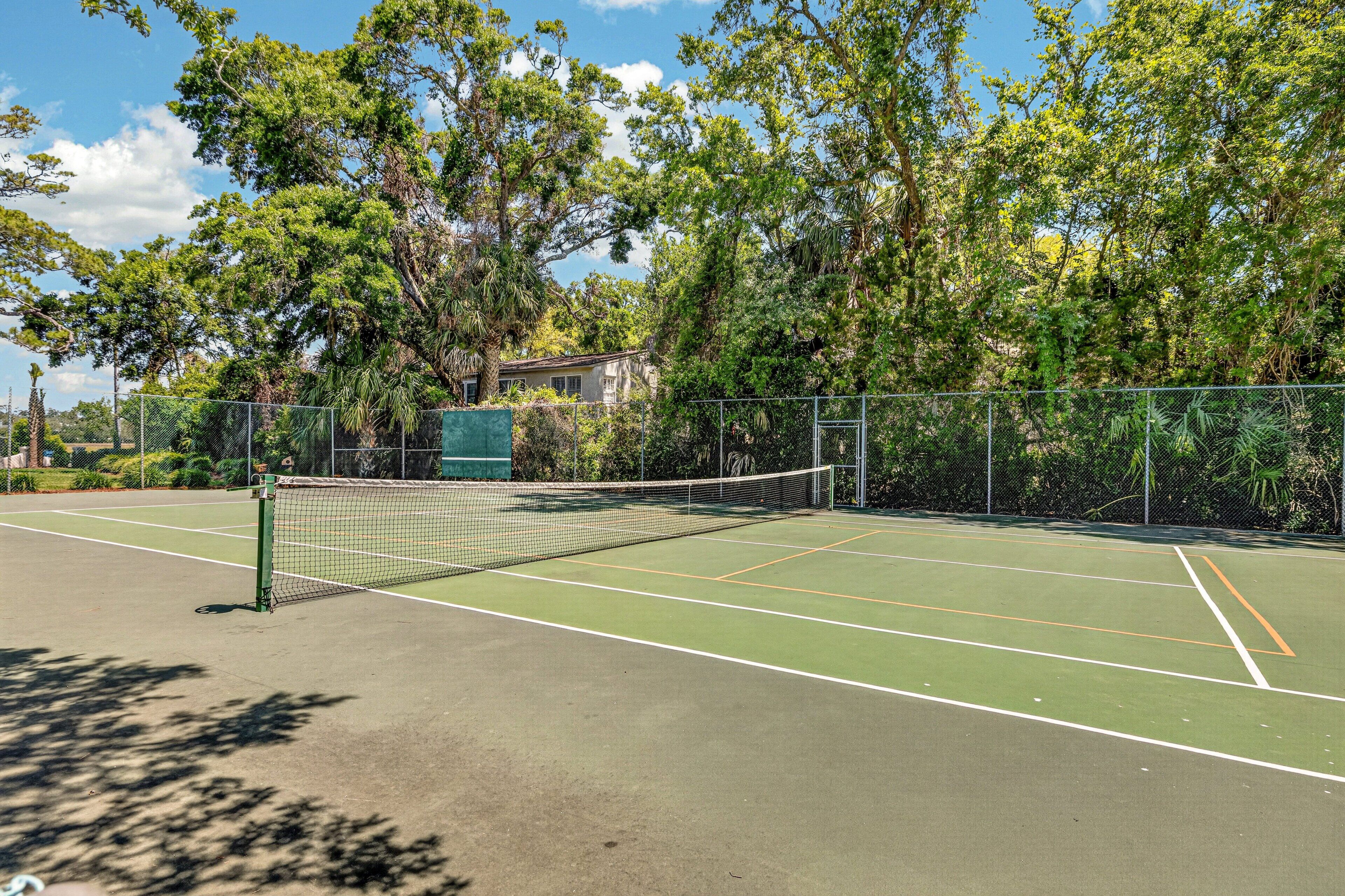 A tennis court with a net, surrounded by trees and a building in the background.