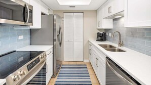 Una cocina moderna con armarios blancos, un refrigerador de acero inoxidable, un microondas integrado, una estufa a gas, un lavavajillas y un tapete azul a rayas.