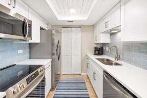 A modern kitchen with white cabinets, a stainless steel refrigerator, a built-in microwave, a gas stove, a dishwasher, and a blue striped rug. - Oceanfront Condominium with Great Amenities (Saint Simons Island)