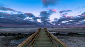 Un muelle de madera que lleva a una playa bajo un cielo nublado.