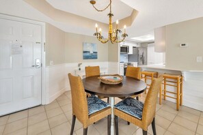 A dining area with a round table, wicker chairs, and a chandelier. - Oceanfront Condominium with Great Amenities (Saint Simons Island)