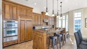 A spacious kitchen with wooden cabinets, stainless steel appliances, and a central island with bar stools. - Luxurious Complex. Steps from the Beach! (Saint Simons Island)