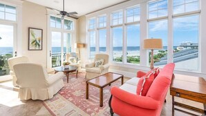 A spacious living room with large windows, a ceiling fan, and a view of the ocean. - Luxurious Complex. Steps from the Beach! (Saint Simons Island)