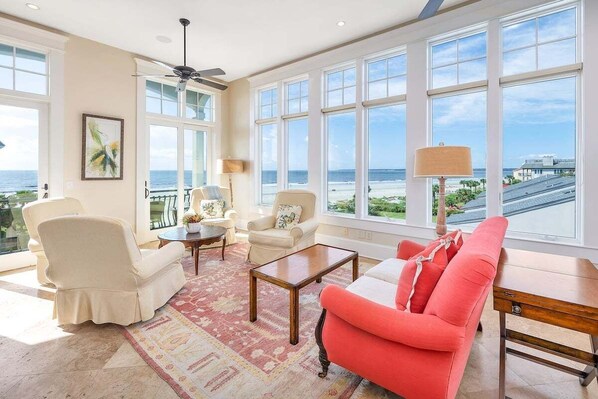 A spacious living room with large windows, a ceiling fan, and a view of the ocean.