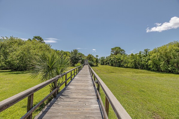 A wooden boardwalk leading through a grassy area with trees on both sides. - Bright St. Simons Condo Near Beach & Dining (Saint Simons Island)