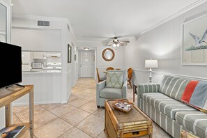 A living room with a television, a sofa, a chair, a lamp, and a decorative wall piece.