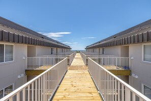 A corridor leading to a row of beachside cabins with a wooden deck and white railings. - Bright St. Simons Condo Near Beach & Dining (Saint Simons Island)