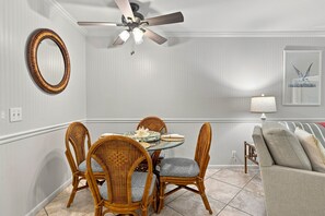 A dining area with a round table, four wicker chairs, a ceiling fan, a wall-mounted mirror, and a framed picture. - Bright St. Simons Condo Near Beach & Dining (Saint Simons Island)