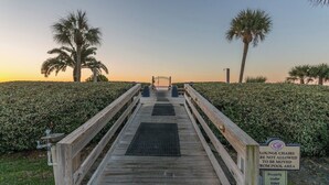 A wooden boardwalk leading to a pool area with lounge chairs, palm trees, and a sign indicating surveillance. - Oceanfront Resort with Pool, Tennis and Fitness Ce (Saint Simons Island)