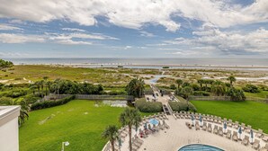 A pool area with lounge chairs and umbrellas, a well-maintained lawn, and a view of the beach and ocean. - Oceanfront Condo with community pool! (Saint Simons Island)