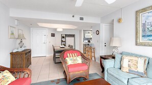 A living room with a dining area, a kitchen in the background, and a large window. - Oceanfront Condo with community pool! (Saint Simons Island)
