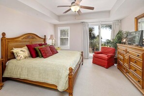 A bedroom with a large bed, a red chair, a wooden dresser, and a ceiling fan.