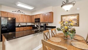 Cozinha moderna com armários de madeira, uma geladeira preta e um espaço de jantar com mesa e cadeiras de madeira.