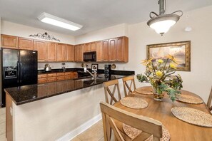 A modern kitchen with wooden cabinets, a black refrigerator, and a dining area with a wooden table and chairs.