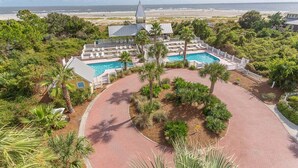A resort with a swimming pool, palm trees, and a view of the beach. - Cottage Steps from the Beach with Community Pool (Saint Simons Island)