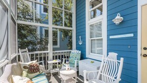 A sunlit porch with wicker furniture, a small table, and a sign reading "WELCOME TO THE BEACH". - Cottage Steps from the Beach with Community Pool (Saint Simons Island)
