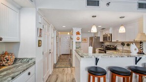 A modern kitchen with white cabinetry, a marble countertop, and a central island with bar stools. - Oceanfront Condominium with Great Amenities! (Saint Simons Island)