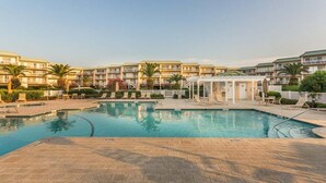 Un espace piscine avec des chaises longues, un petit kiosque et un bâtiment doté de plusieurs balcons en arrière-plan.