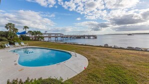 A swimming pool with lounge chairs, a pier extending into the water, and a clear sky. - First Floor Oceanfront Condominium in the Heart of (Saint Simons Island)