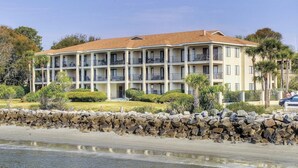 A multi-story hotel with balconies, located near a beach with a stone wall and greenery. - First Floor Oceanfront Condominium in the Heart of (Saint Simons Island)