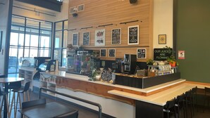 Een modern café met een wand van hout, een toonbank met een koffiemachine en een bord waarop siroop smaken worden aangeboden.