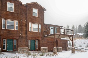 Un grand bâtiment en bois, doté de nombreuses fenêtres et portes, d’une fondation en pierre et d’un balcon en bois.