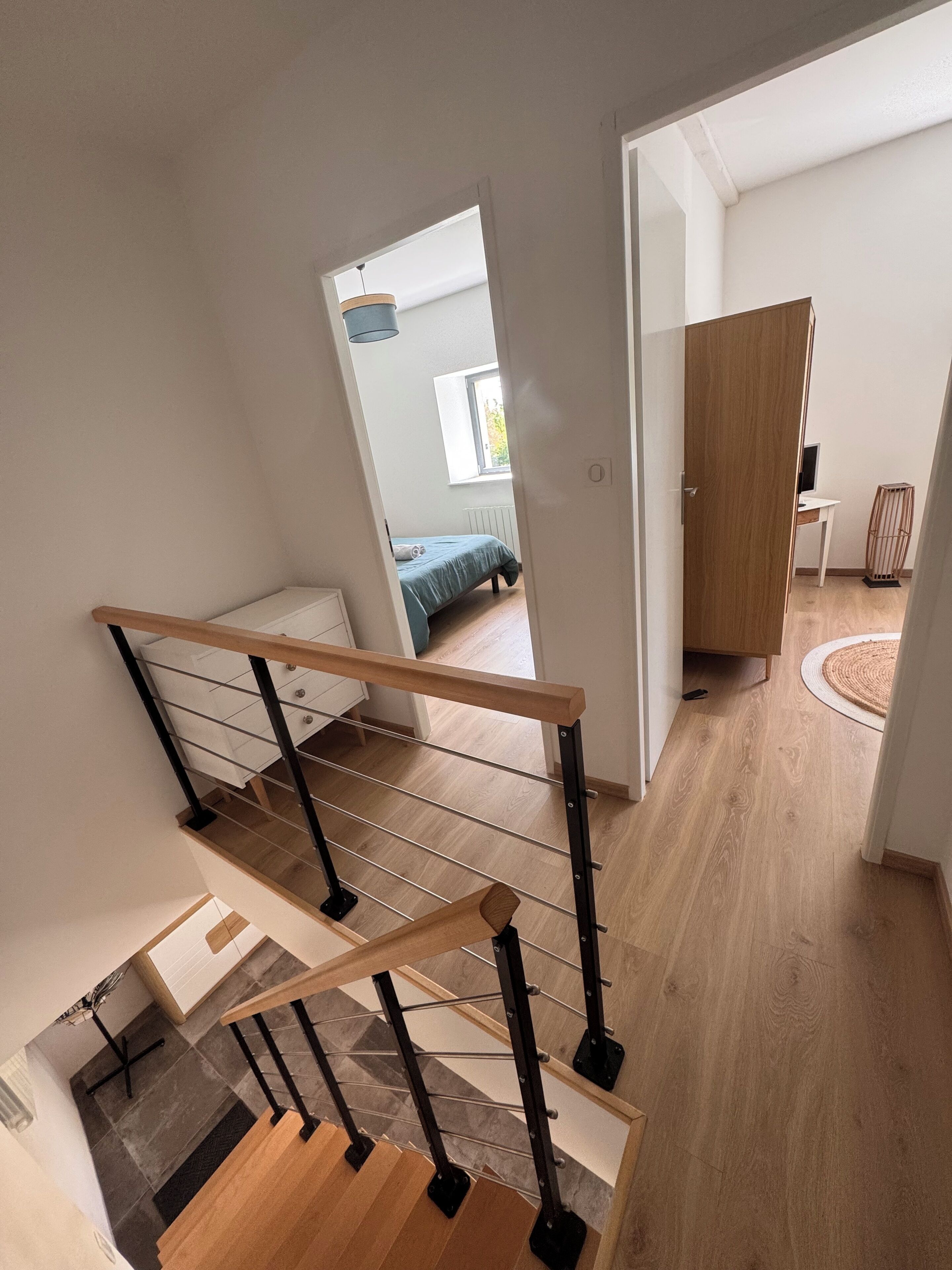 Ein modernes Interieur mit einer Holztreppe, einem Bett im angrenzenden Raum und einem Schreibtisch mit einem Computer.