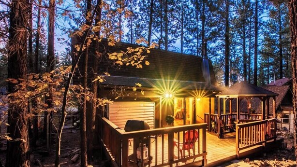 Una cabaña con terraza de madera, porche cubierto y un pequeño espacio exterior para sentarse.