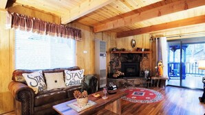 Acogedor interior de cabaña de madera con chimenea, pisos de madera, un sofá de cuero y una mesa de comedor.