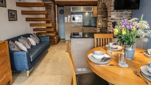 A modern kitchen with a built-in oven and microwave, a dining area with a wooden table set for two, and a staircase leading to an upper level. - Swallows Nest (Whitby)