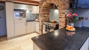 A modern kitchen with white cabinets, a black countertop, and a brick archway. - Swallows Nest (Whitby)