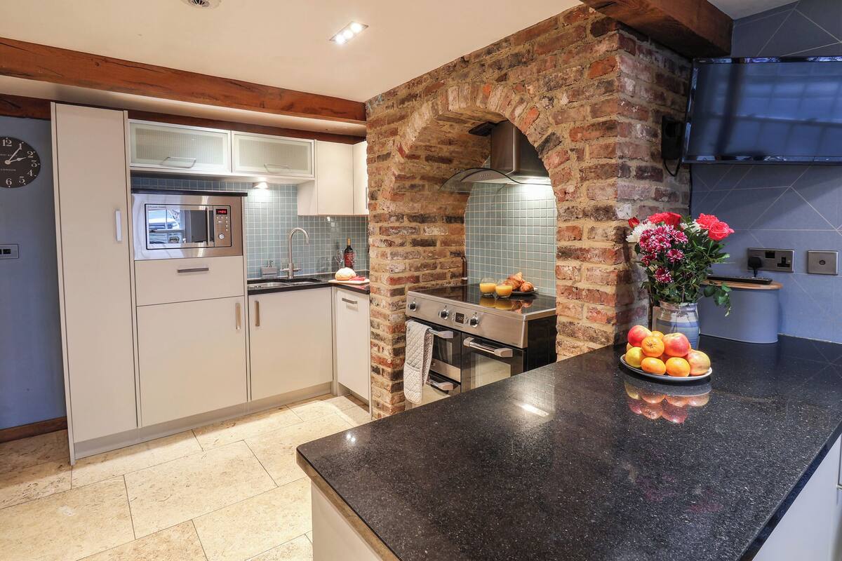 A modern kitchen with white cabinets, a black countertop, and a brick archway.