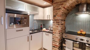 A modern kitchen with stainless steel appliances, a brick archway, and blue-tiled backsplash. - Swallows Nest (Whitby)