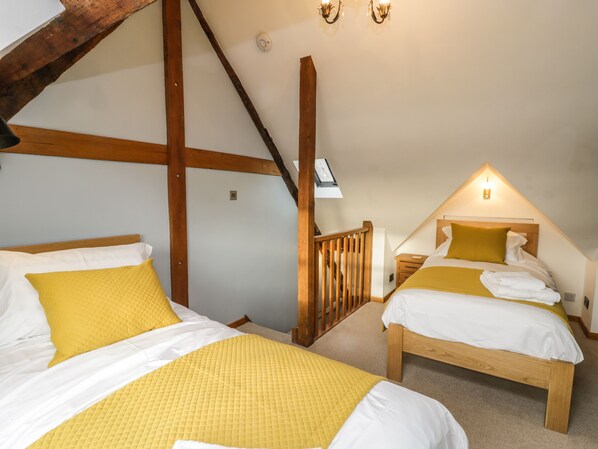 A bedroom with two beds, wooden beams, a sloped ceiling, and a skylight. - Swallows Nest (Whitby)