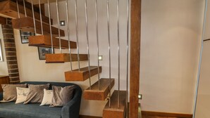 A modern living room with a blue sofa, wooden staircase, and a brick wall. - Swallows Nest (Whitby)