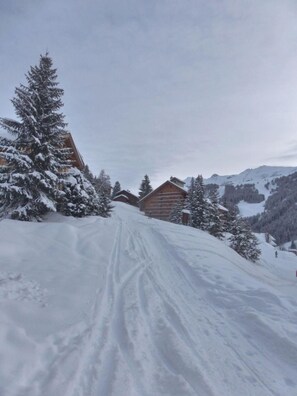 A snow-covered mountain path leading to wooden cabins with a forest backdrop. - Ski-in/ski-out & foot of the slopes, 4th floor, view mountain/ski slopes, balcony (Méribel - Les Allues)