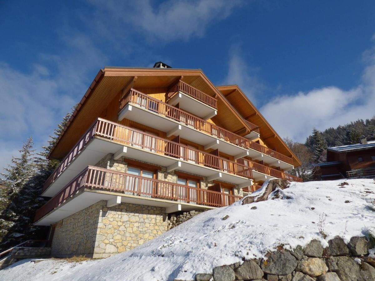 Un chalet à plusieurs étages, doté de balcons en bois, de fondations en pierre et surplombant un paysage enneigé.