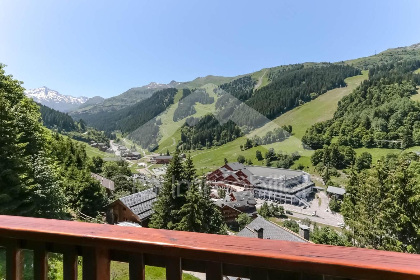 Ein Bergdorf mit traditionellen Holzbauten, einem klaren Himmel und einem Tal mit einer Skipiste.
